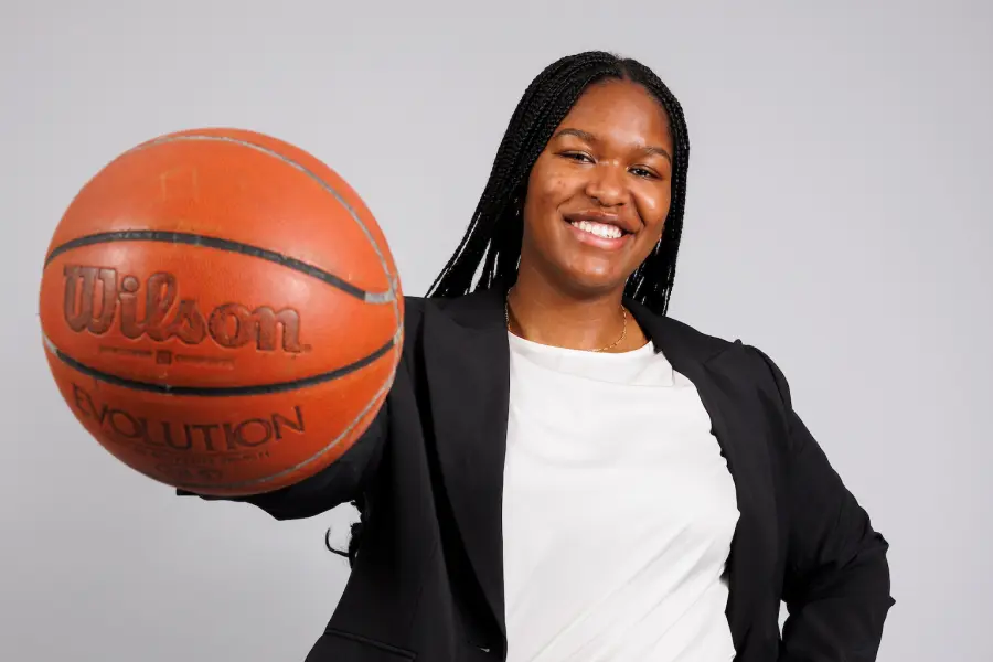 A female student wearing a suite holds a basketball in one hand up to the camera.