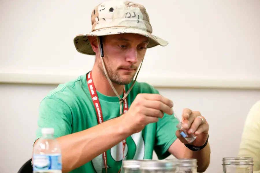 A man wearing a bucket hat holds a tub of water in front of him.