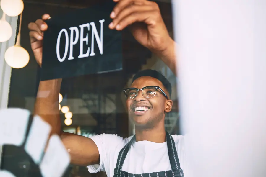 A man wearing an apron is switching an open sign through a store window.