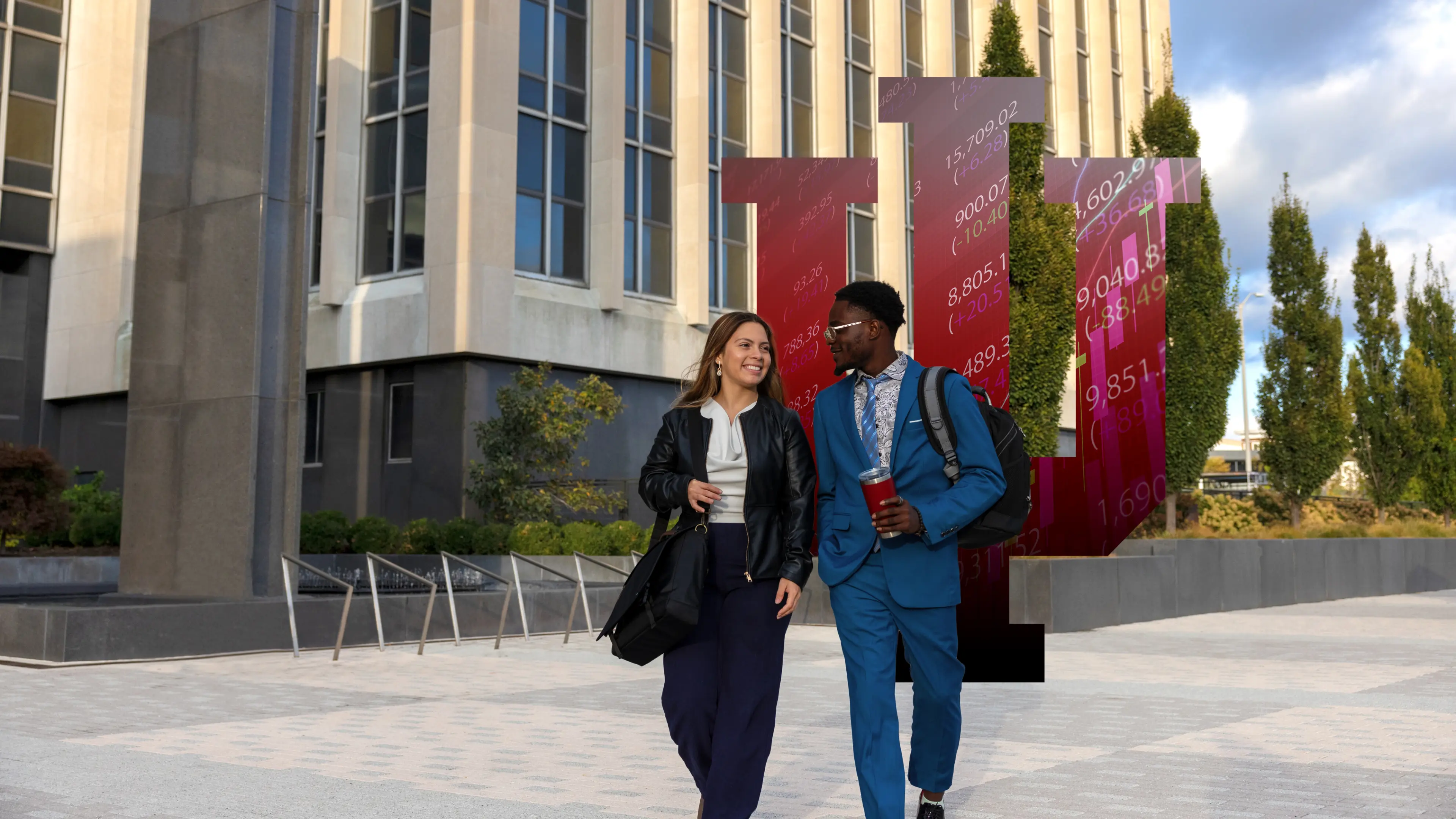 Two students walk on campus while in conversation. An IU trident appears behind them containing numbers and equations.
