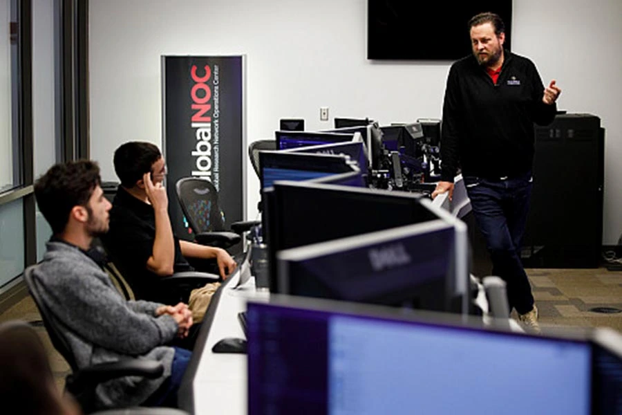 Workers at a network operations center discuss operations.