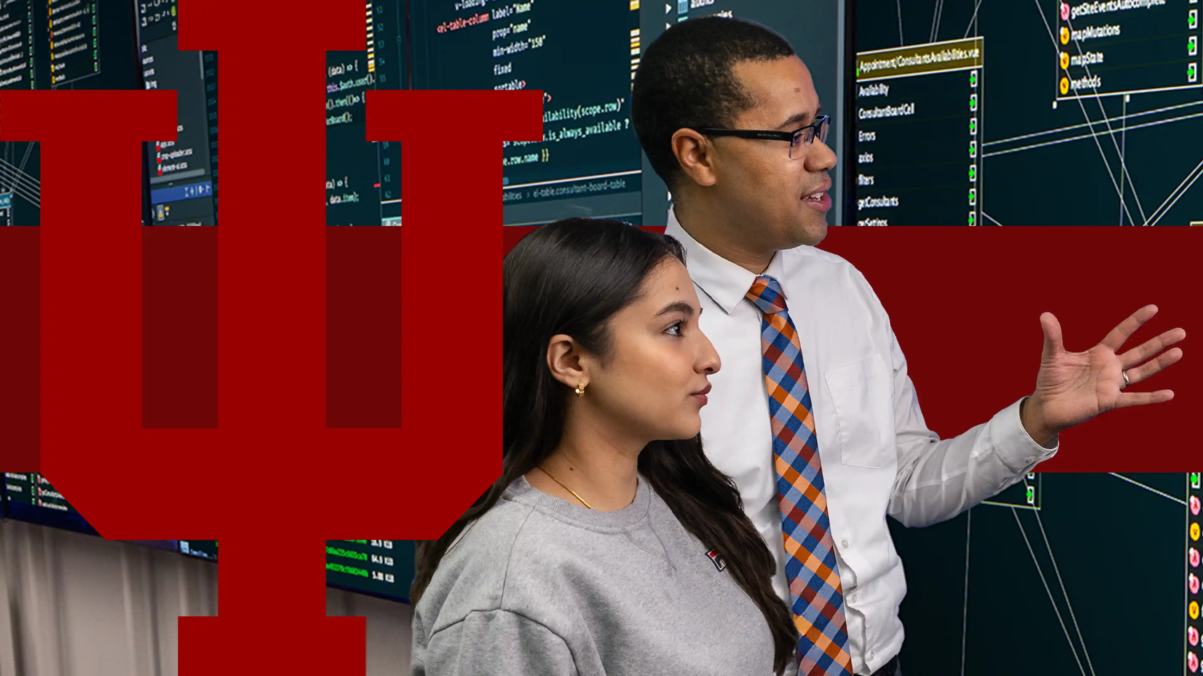 A male professor explains a large screen of cybersecurity flowcharts to a female student, listening intently.