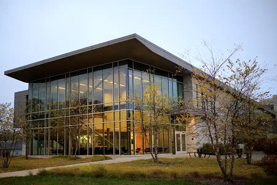 A large, modern glass building lit with gold lighting at dusk.