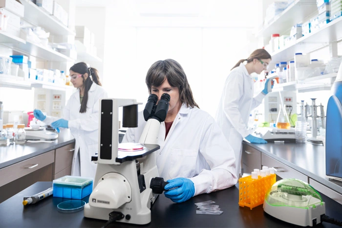A researcher wearing a lab coat looks through a microscope.