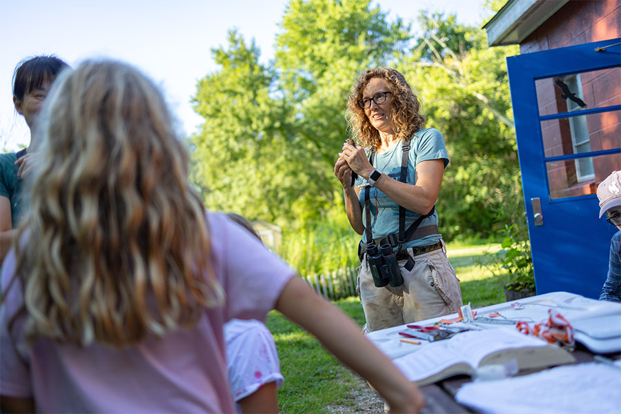 A teacher speaks to students outside on a sunny day about nature.