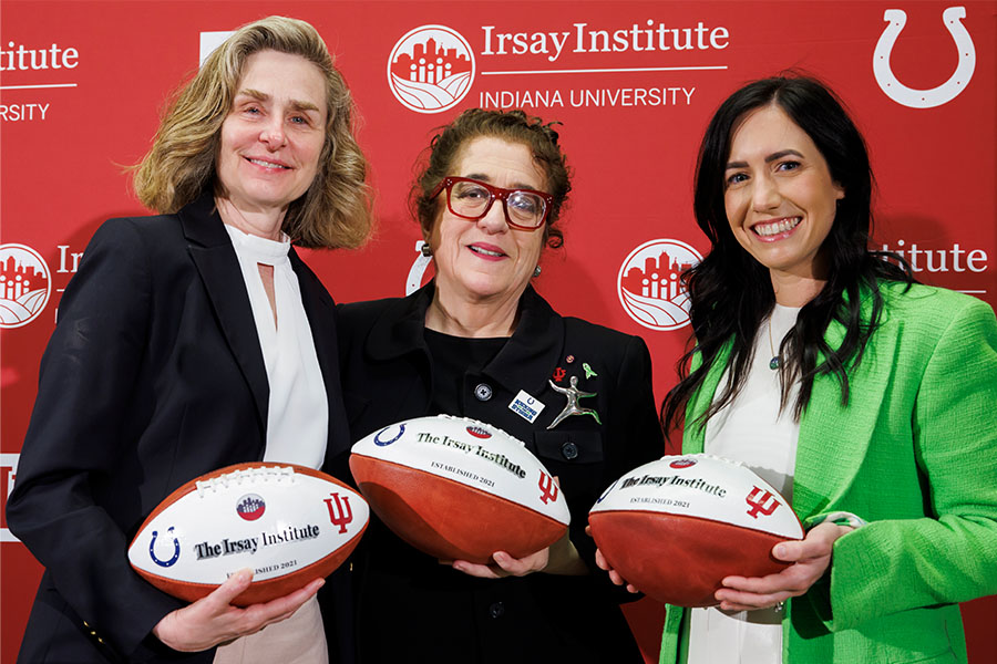 IU president Pamela Whitten stands with two other woman holding footballs with the Irsay Institute logo on them.